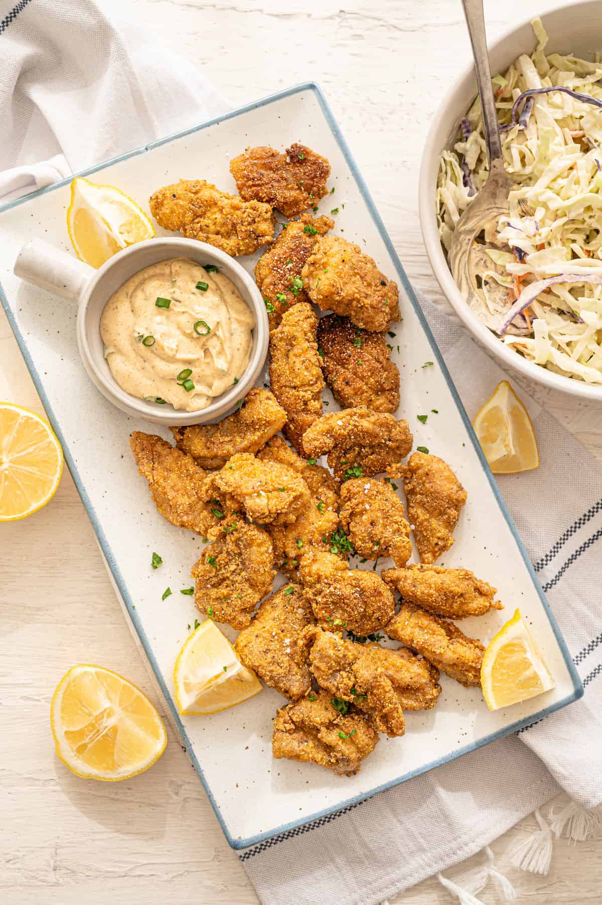 Fried catfish nuggets on a platter with lemons and remoulade sauce with coleslaw on the side.