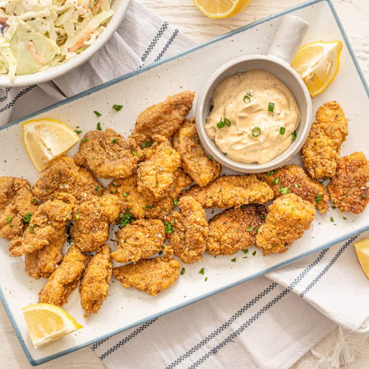 fried catfish nuggets on a platter with lemons and remoulade sauce