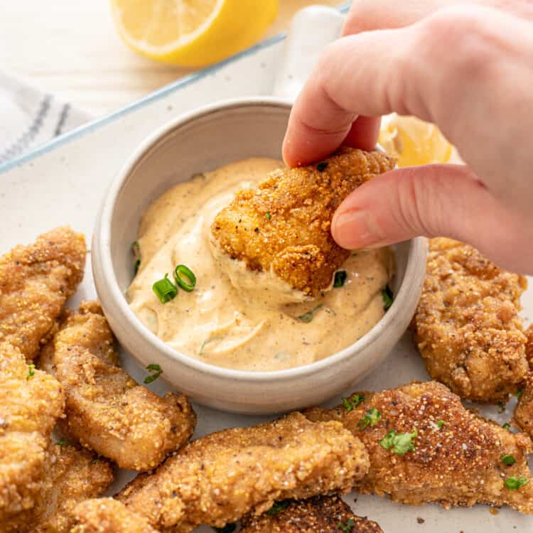 A catfish nugget being dipped in cajun remoulade sauce.