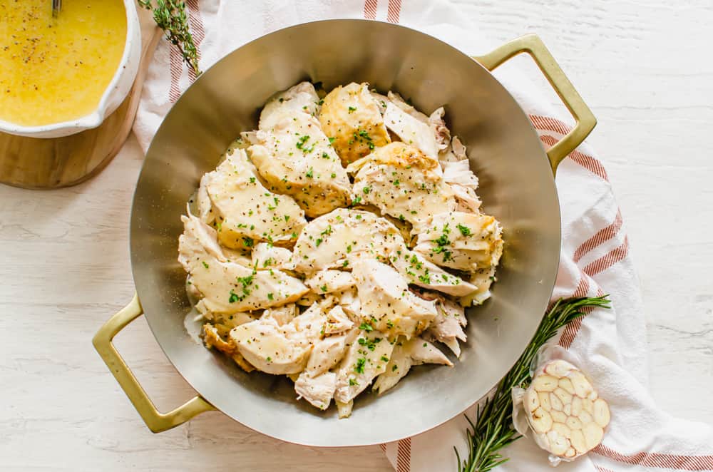 Chicken sliced from whole chicken on a serving platter with a full gravy boat nearby.