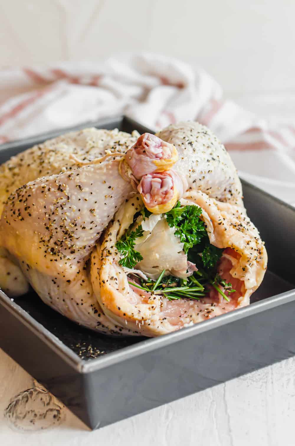 Raw, seasoned whole chicken stuffed with herbs and vegetables in a baking pan.