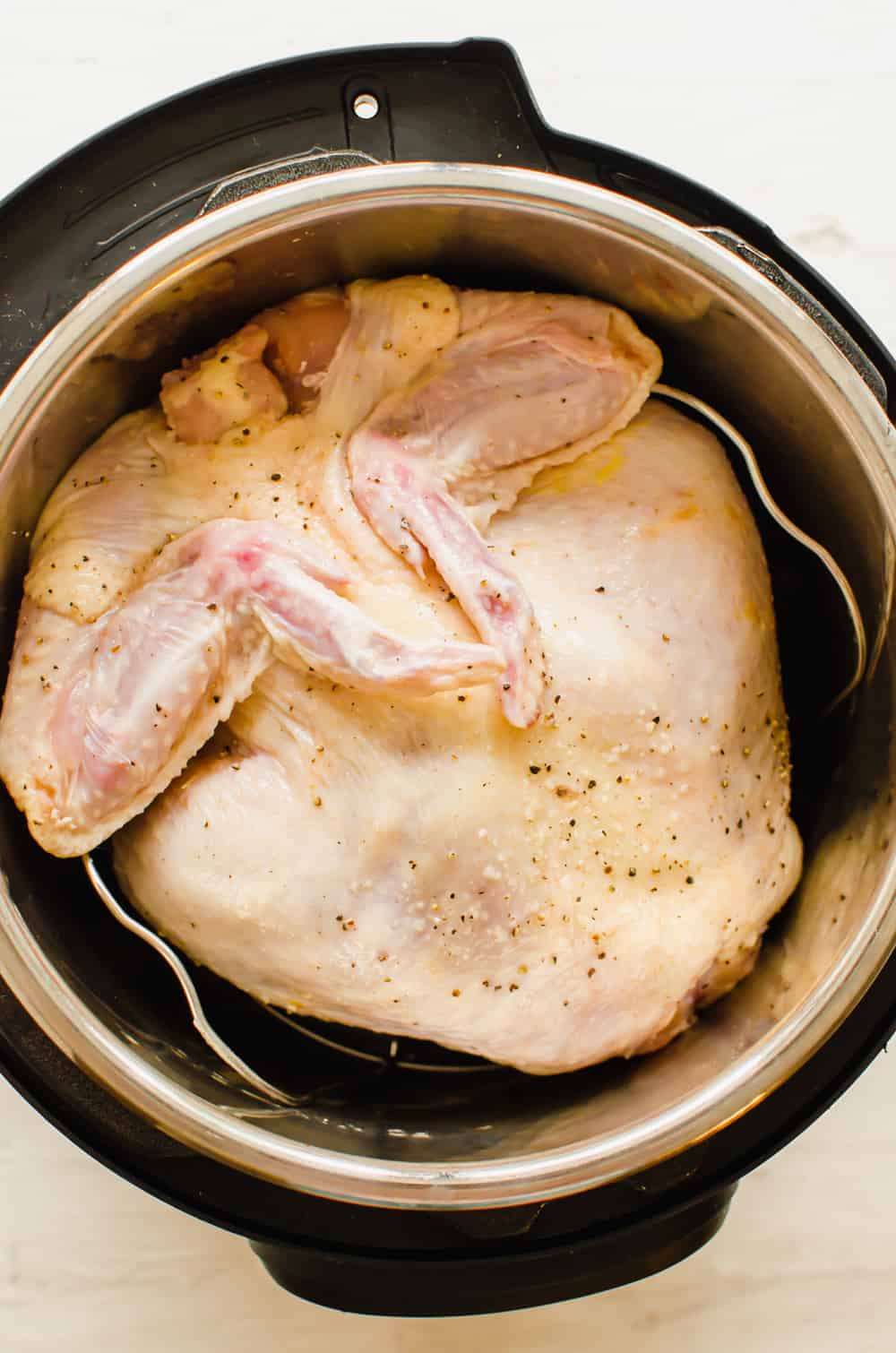 A whole, raw chicken in an instant Pot with seasonings on it.