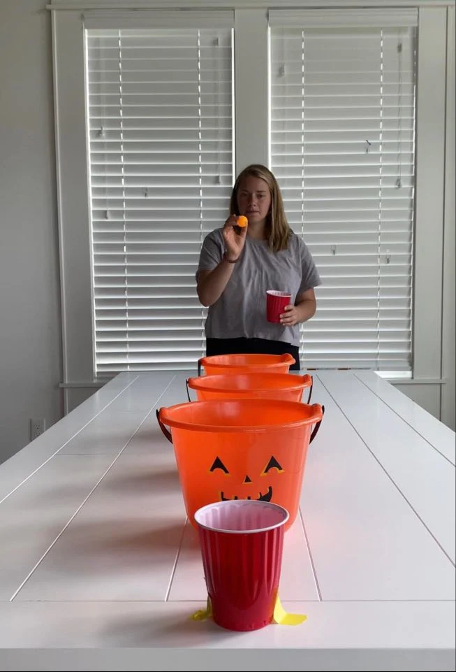 Person about to bounce a ping pong ball on a table trying to get it into plastic pumpkins.