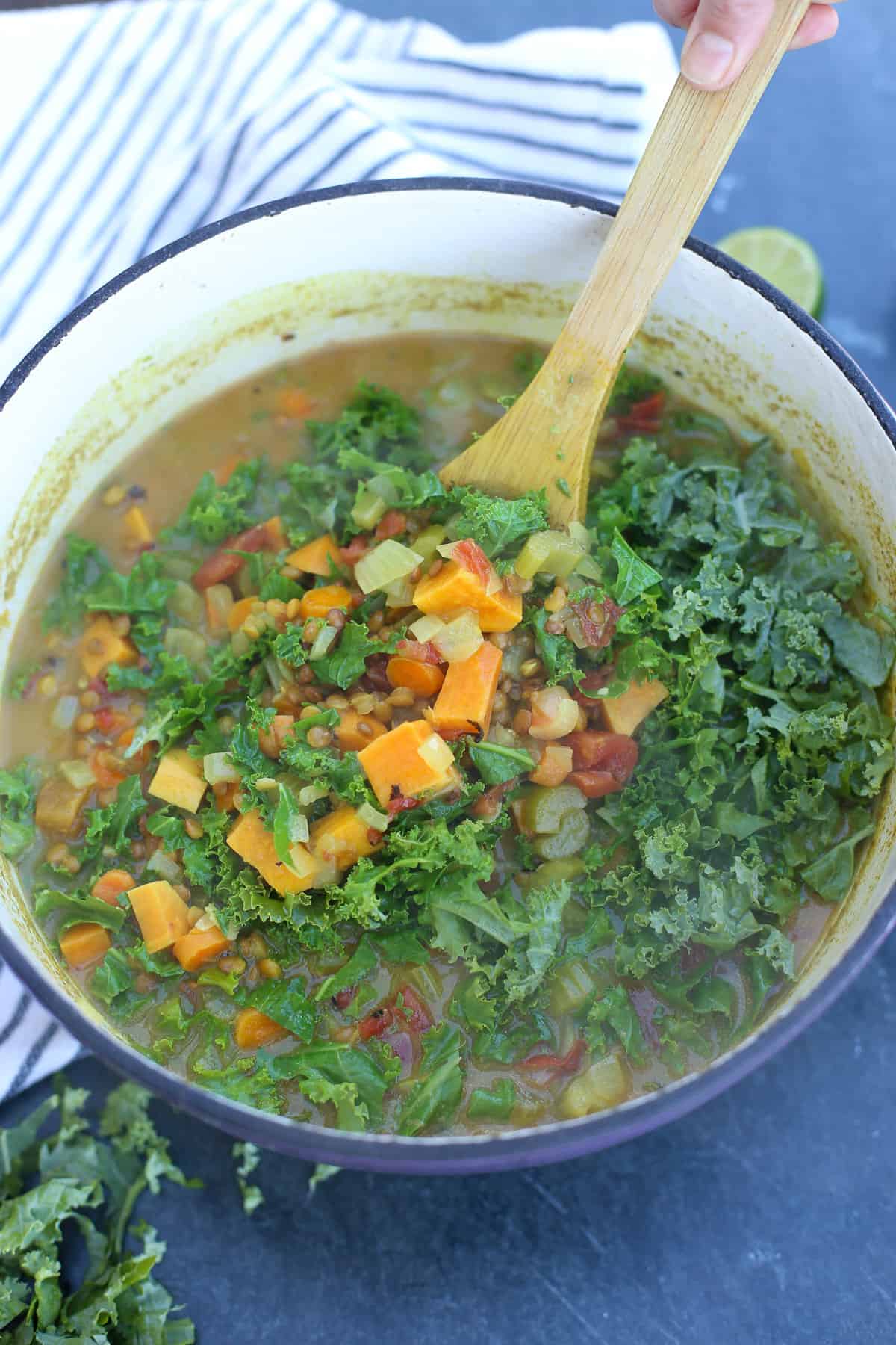 Stirring chopped kale into coconut curry soup with a wooden spoon.