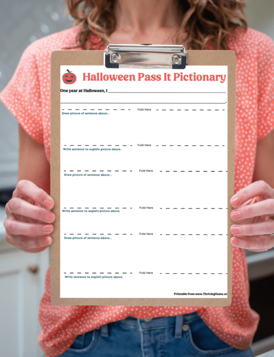 Hands holding a clipboard with a Halloween Pass It Pictionary printable on it.