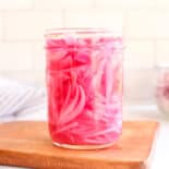 Pickled red onions in a jar on a counter top.