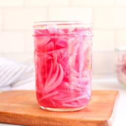 Pickled red onions in a jar on a counter top.