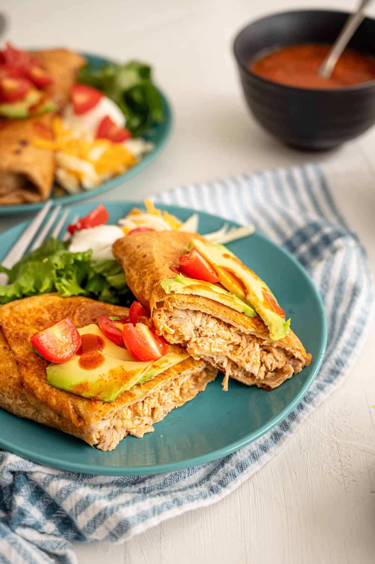 A chicken chimichanga cut in half on an aqua plate with chopped cherry tomatoes, and sliced avocado on top.