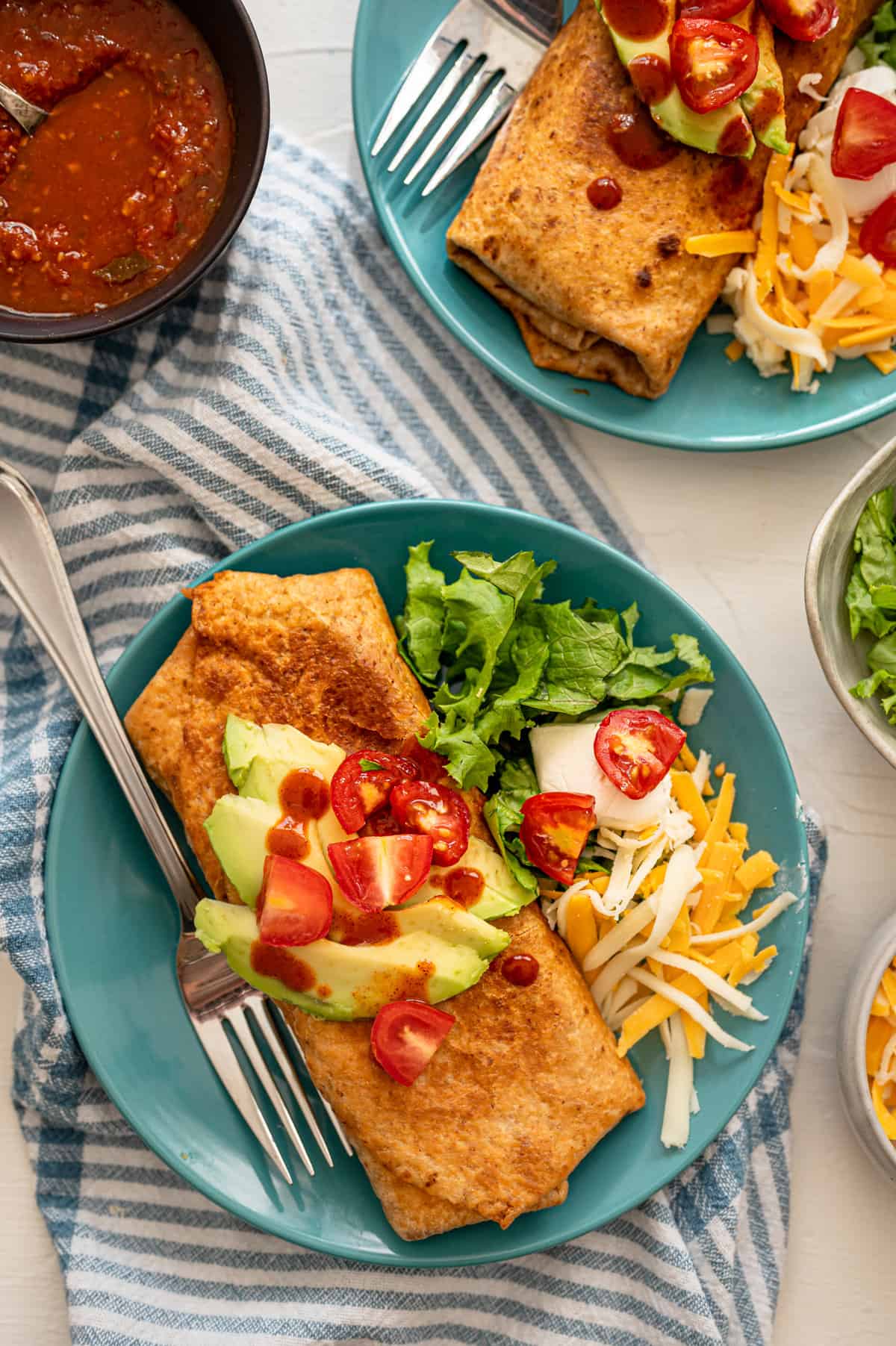 A chicken chimichanga on an aqua plate with avocado slices and chopped cherry tomatoes on top.