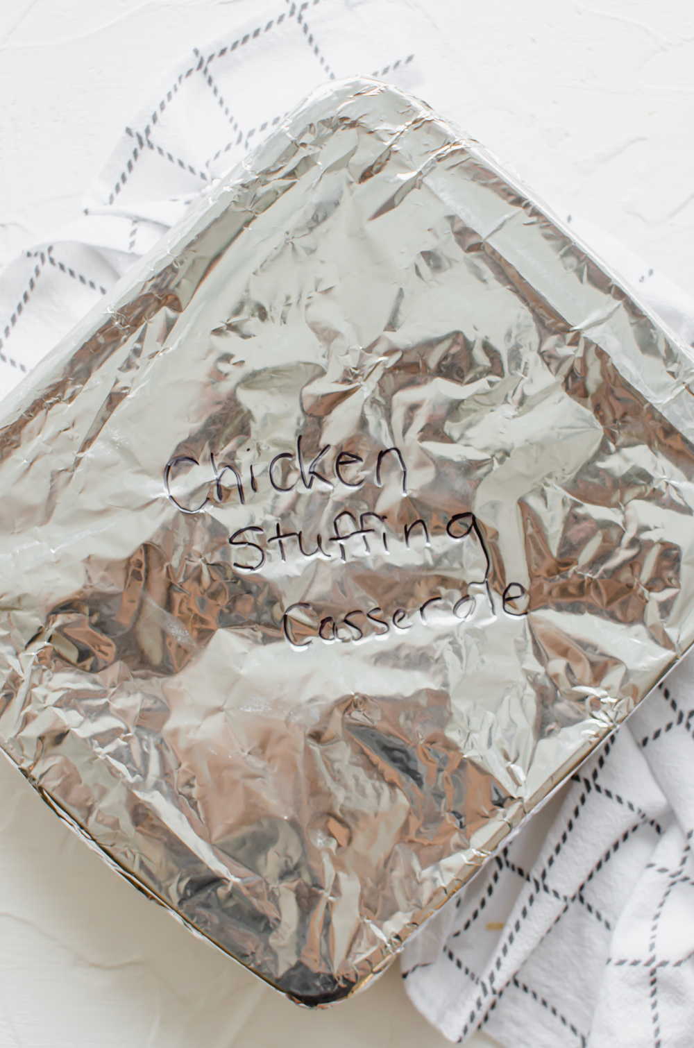 A square casserole dish covered in foil labeled chicken stuffing casserole.