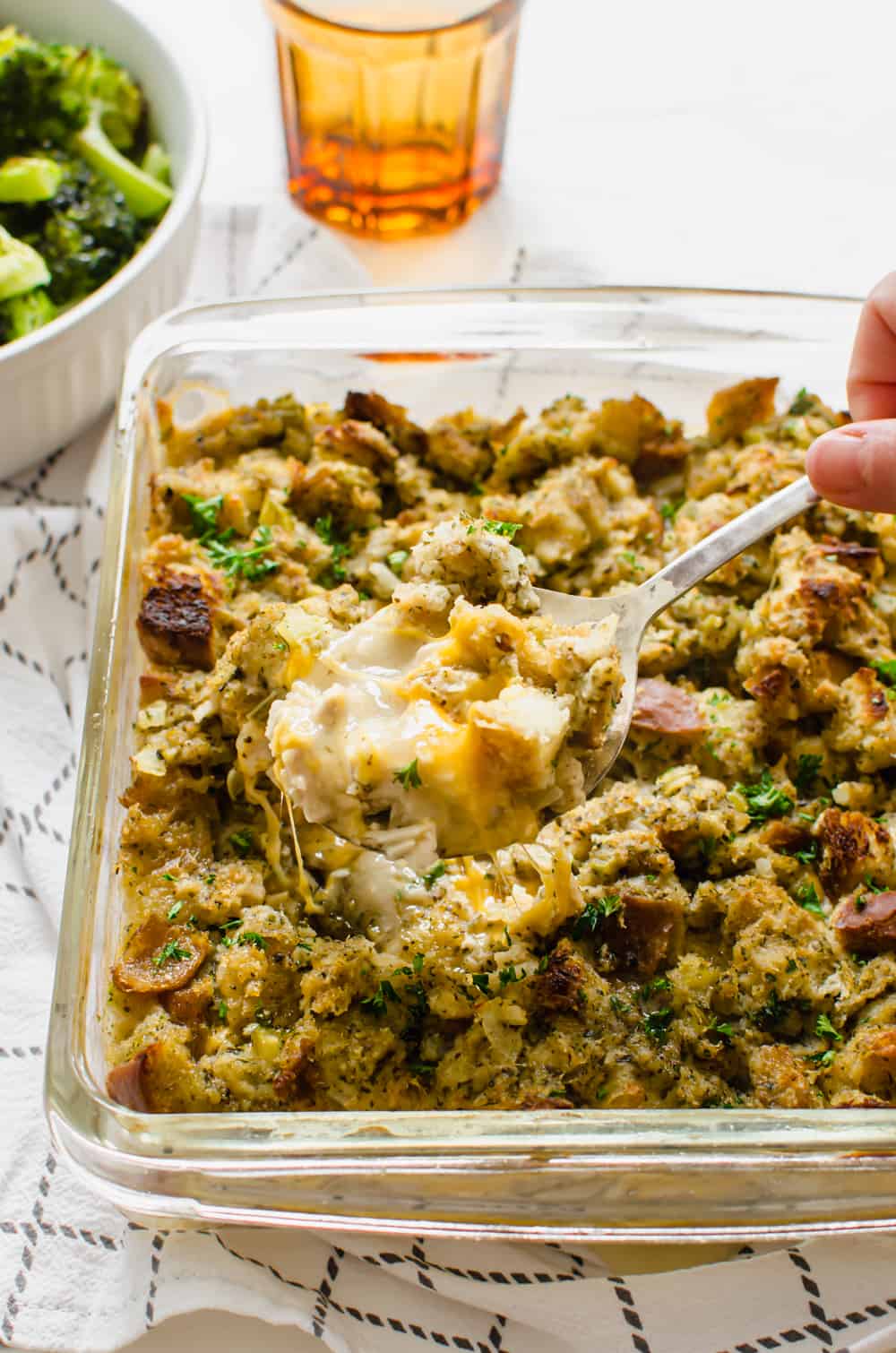 A spoon serving chicken stuffing casserole from a square, glass casserole dish.