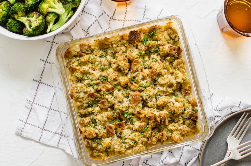 Glass baking dish of ready to serve turkey stuffing casserole with a bowl of roasted broccoli next to it.