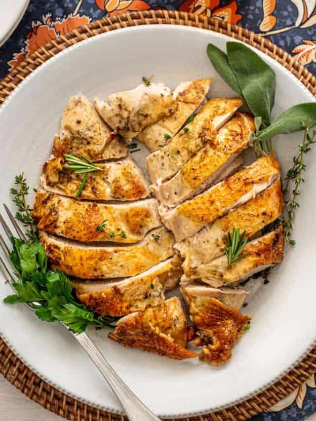 Carved turkey breast on a serving platter with gravy on the side.