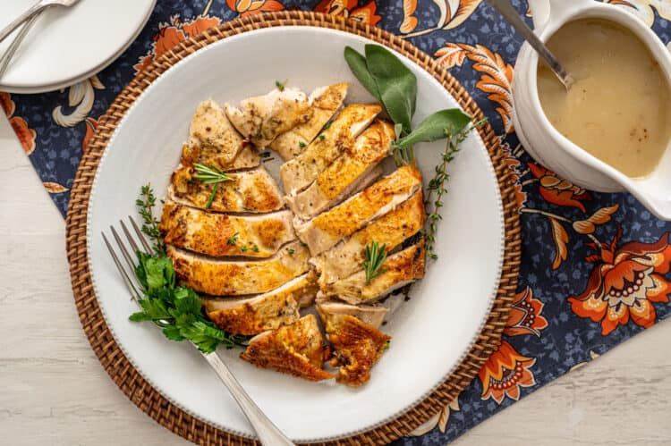 carved turkey breast on a serving platter with gravy on the side