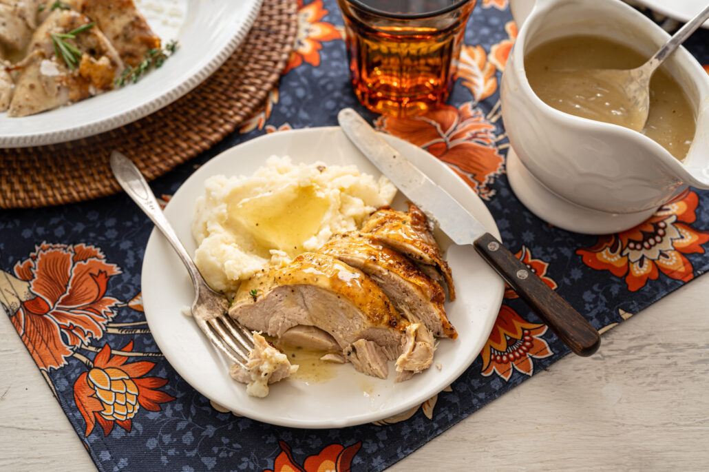 Turkey breast slices and mashed potatoes with gravy on a plate with utensils.