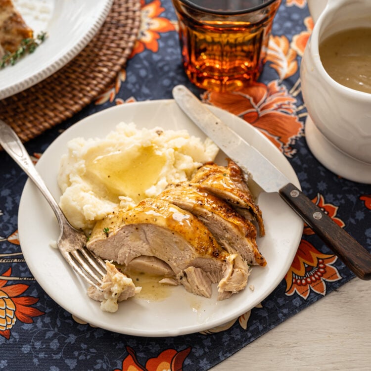 turkey breast slices and mashed potatoes with gravy on a plate with utensils
