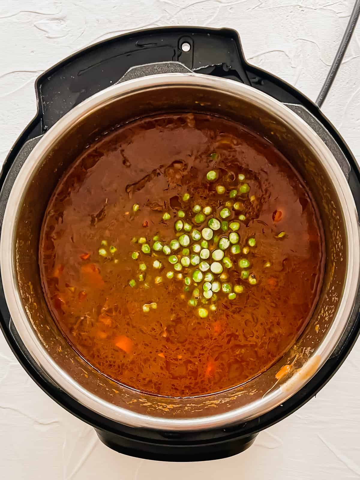 Frozen peas being added to beef stew in an Instant Pot.