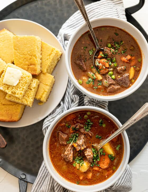 beef stew in bowls with cornbread on a plate nearby.