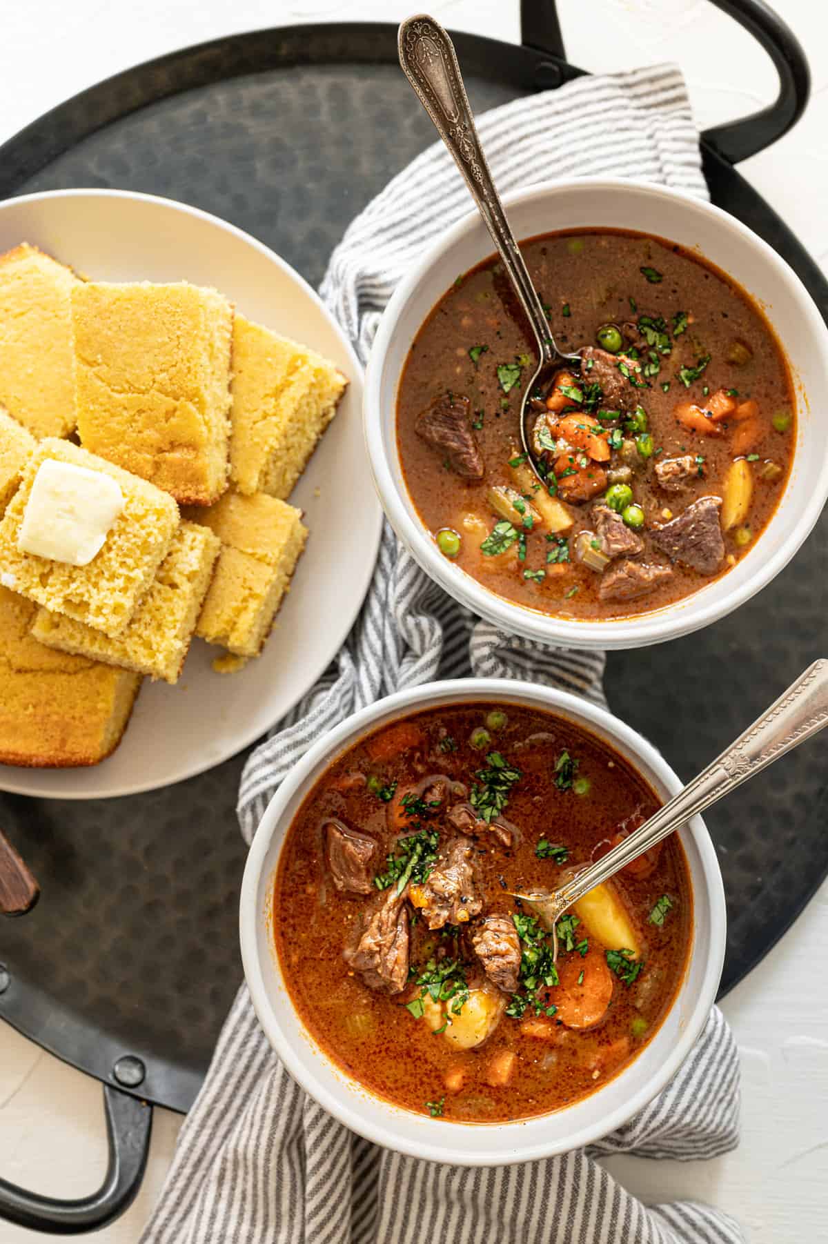 beef stew in bowls with cornbread on a plate nearby.