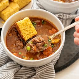 Instant Pot Beef Stew in a bowl with a spoon and a piece of cornbread.