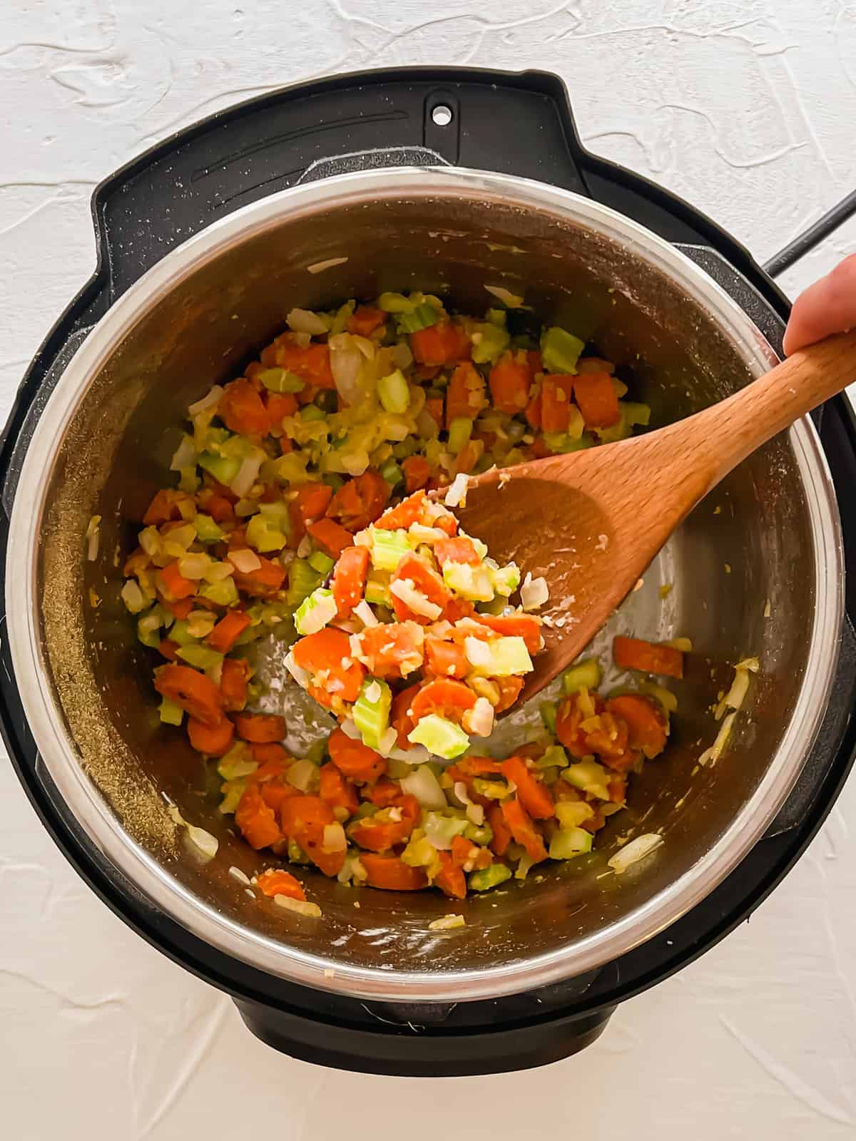 Whole wheat flour being stirred into sauteed carrots, onion, celery and garlic with a wooden spoon.