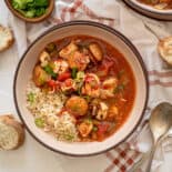 Jambalaya in a bowl served over rice with slices of crusty bread on the table around it.