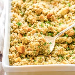 Casserole dish with homemade stuffing and a metal spoon lifting some out.