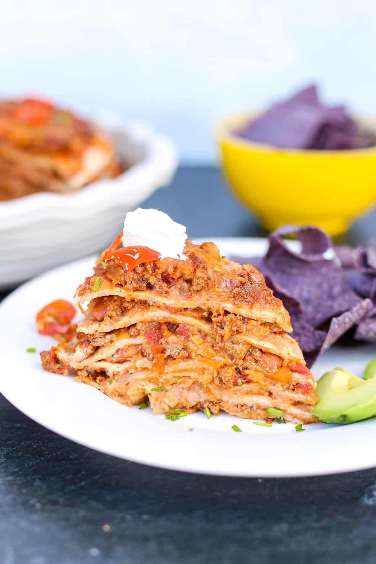 A slice of taco pie with chips and avocado on the side.