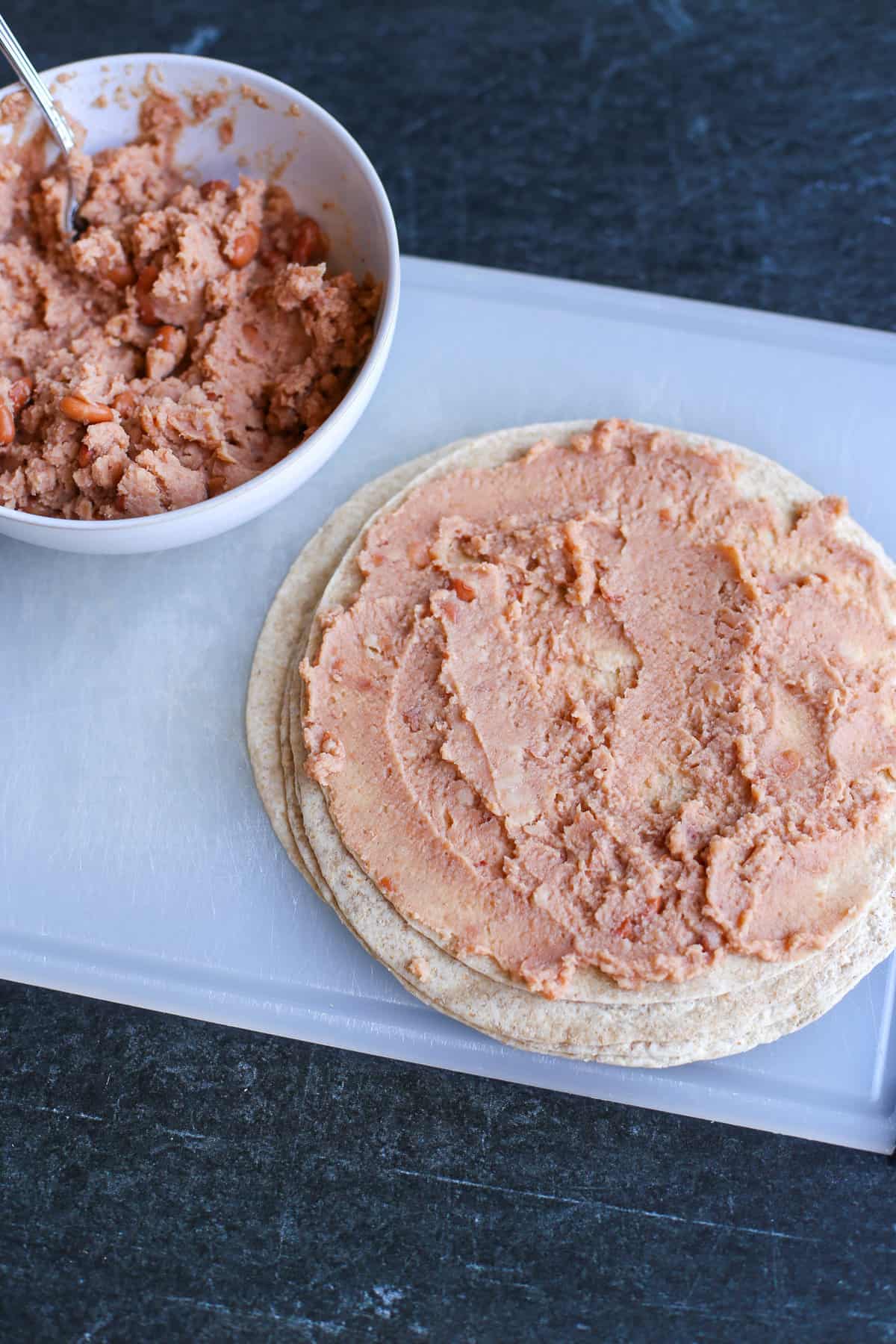 A stack of tortillas with the top having refried beans spread on it.
