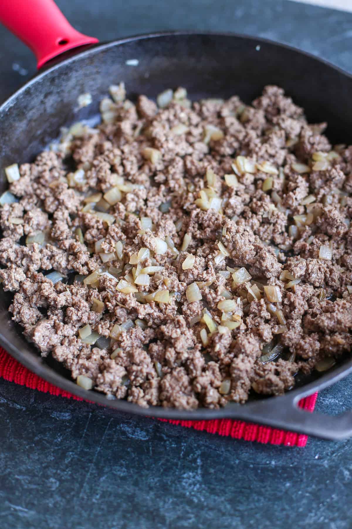 Ground beef and onions cooking in an iron skillet.