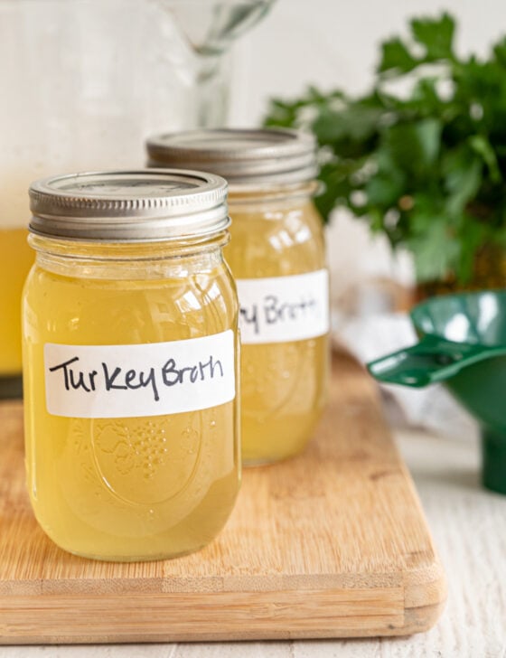 Broth in mason jars labeled turkey broth sealed and sitting on a wooden cutting board.