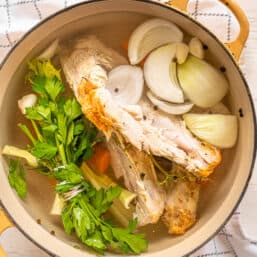 Dutch oven with turkey breast carcass, onions, carrots, celery, garlic cloves, peppercorns, and water to make turkey broth.