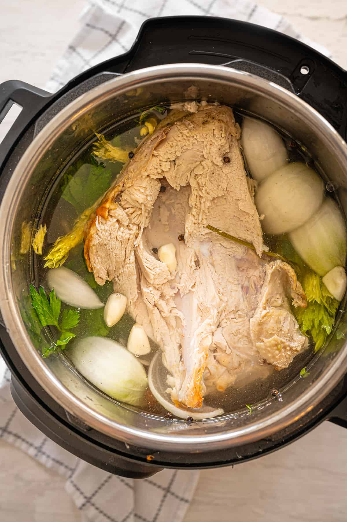 Instant Pot with turkey breast carcass, onions, carrots, celery, garlic cloves, peppercorns, and water to make turkey broth.