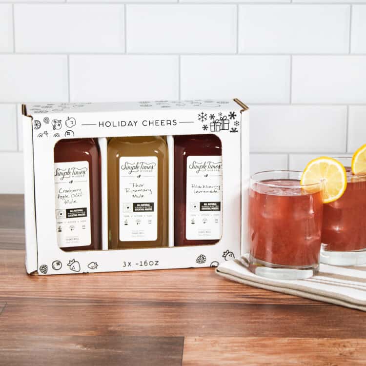 A holiday pack of three Simple Times Mixers with glasses of drinks nearby.