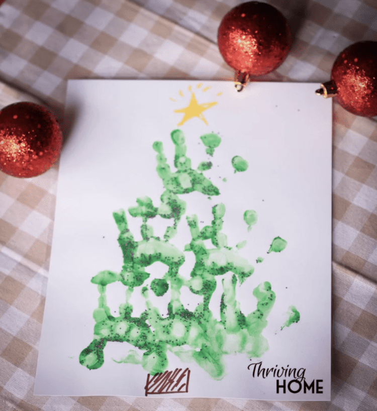 A Christmas tree painting made of little kid hand prints in green and marker-drawn trunk, star, and decorations.
