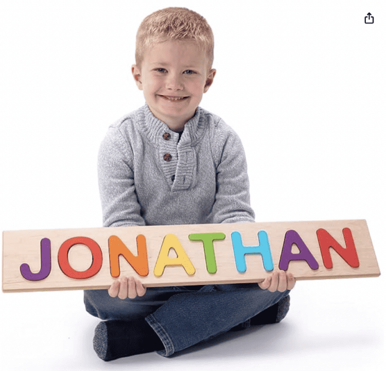 Boy holding his name as a wooden puzzle - the letters are different color and can be taken out and put back in.