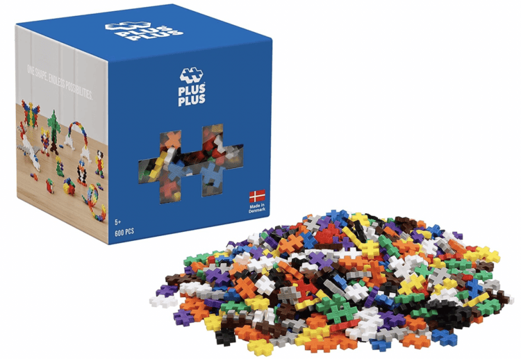 Stock photo of a Plusplus Blocks box with a pile of the blocks in varying colors in front of it.