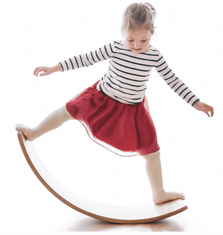 A child standing on a Wooden Wobble Balance Board - a piece of wood bent in an arch shape.