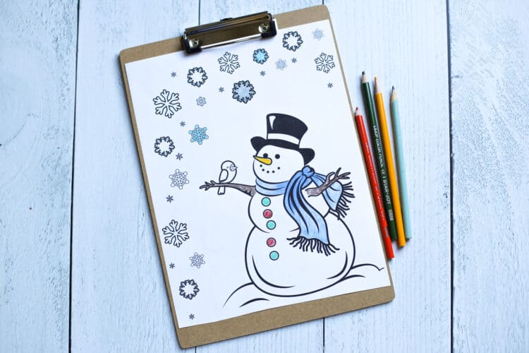 A snowman coloring page partially colored on a clipboard with colored pencils lying near it.