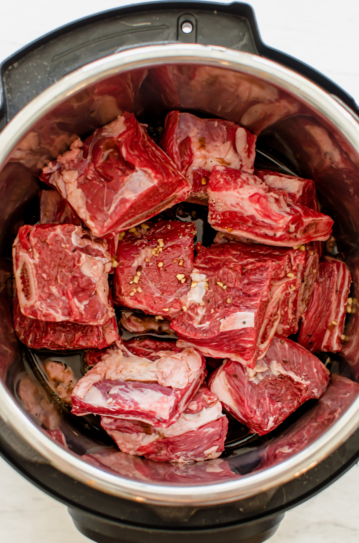 Uncooked beef short ribs cut into 2-inch pieces in an Instant Pot with marinade poured over it.