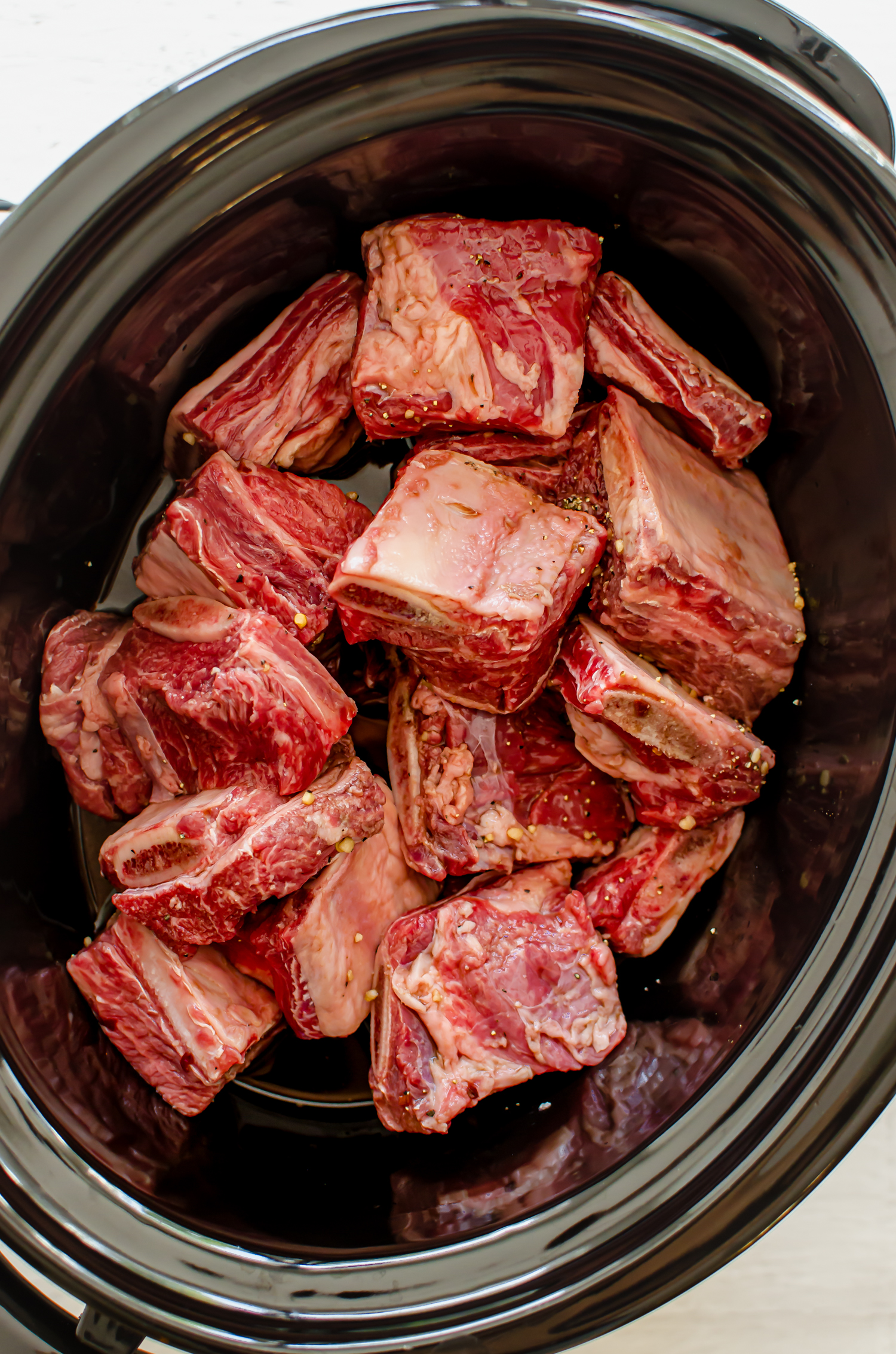 Short ribs in a slow cooker with marinade poured around them.