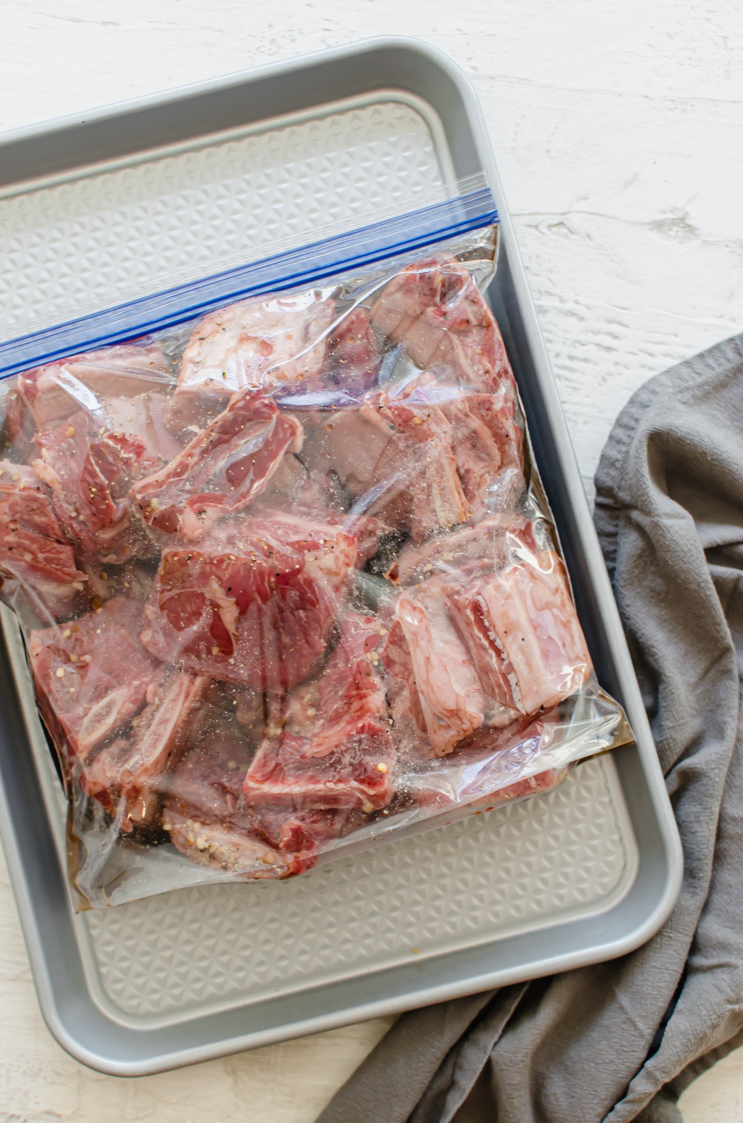Short ribs marinating in a gallon-size bag lying flat on a sheet pan to be frozen.