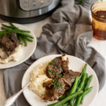 Beef Short Ribs on a plate with mashed potatoes and green beans in front of Instant Pot