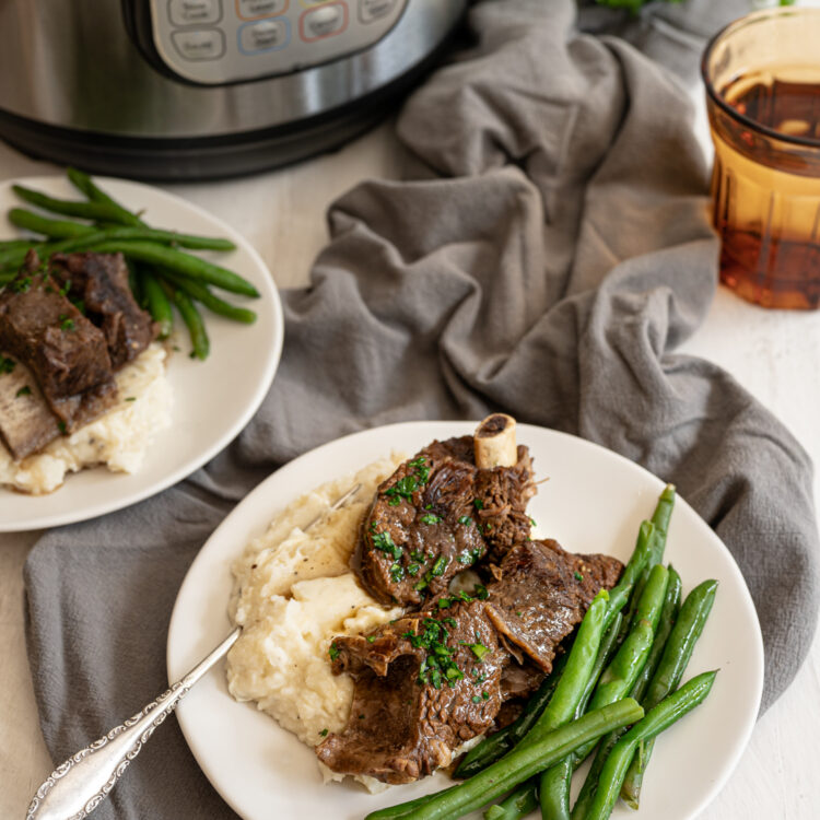 Beef Short Ribs on a plate with mashed potatoes and green beans in front of Instant Pot