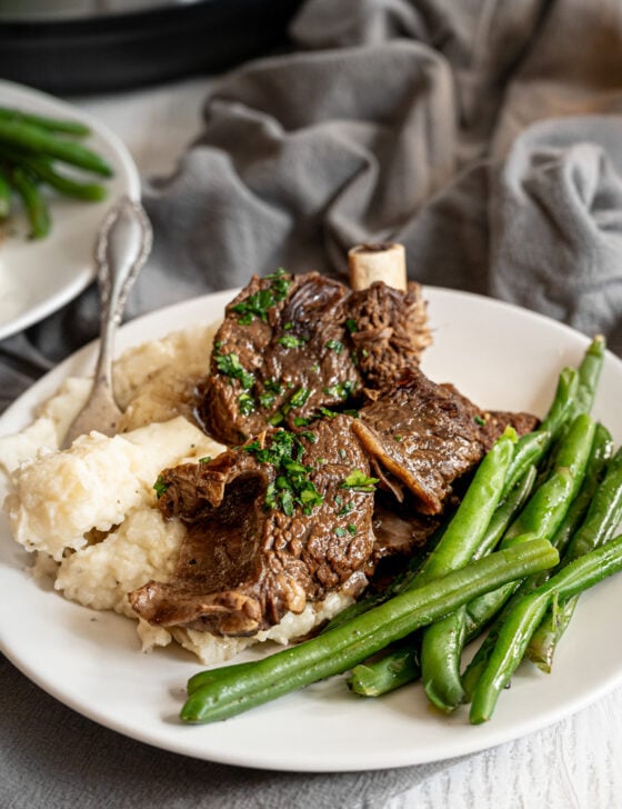 Beef short ribs with mashed potatoes and green beans on a white plate.