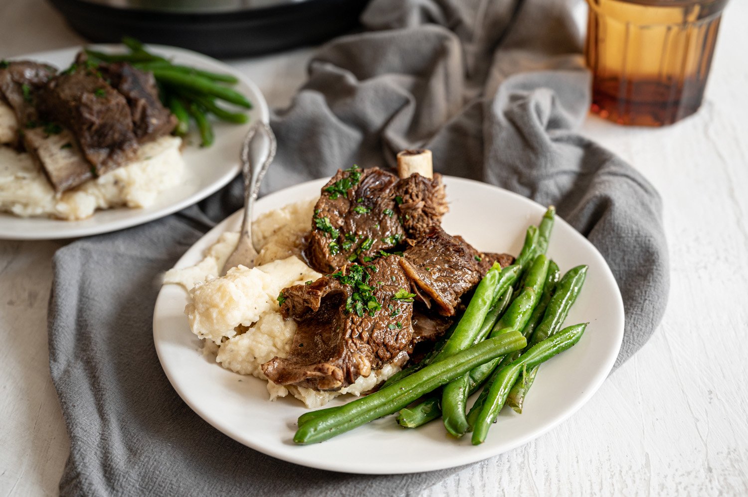 Beef short ribs with mashed potatoes and green beans on a white plate.