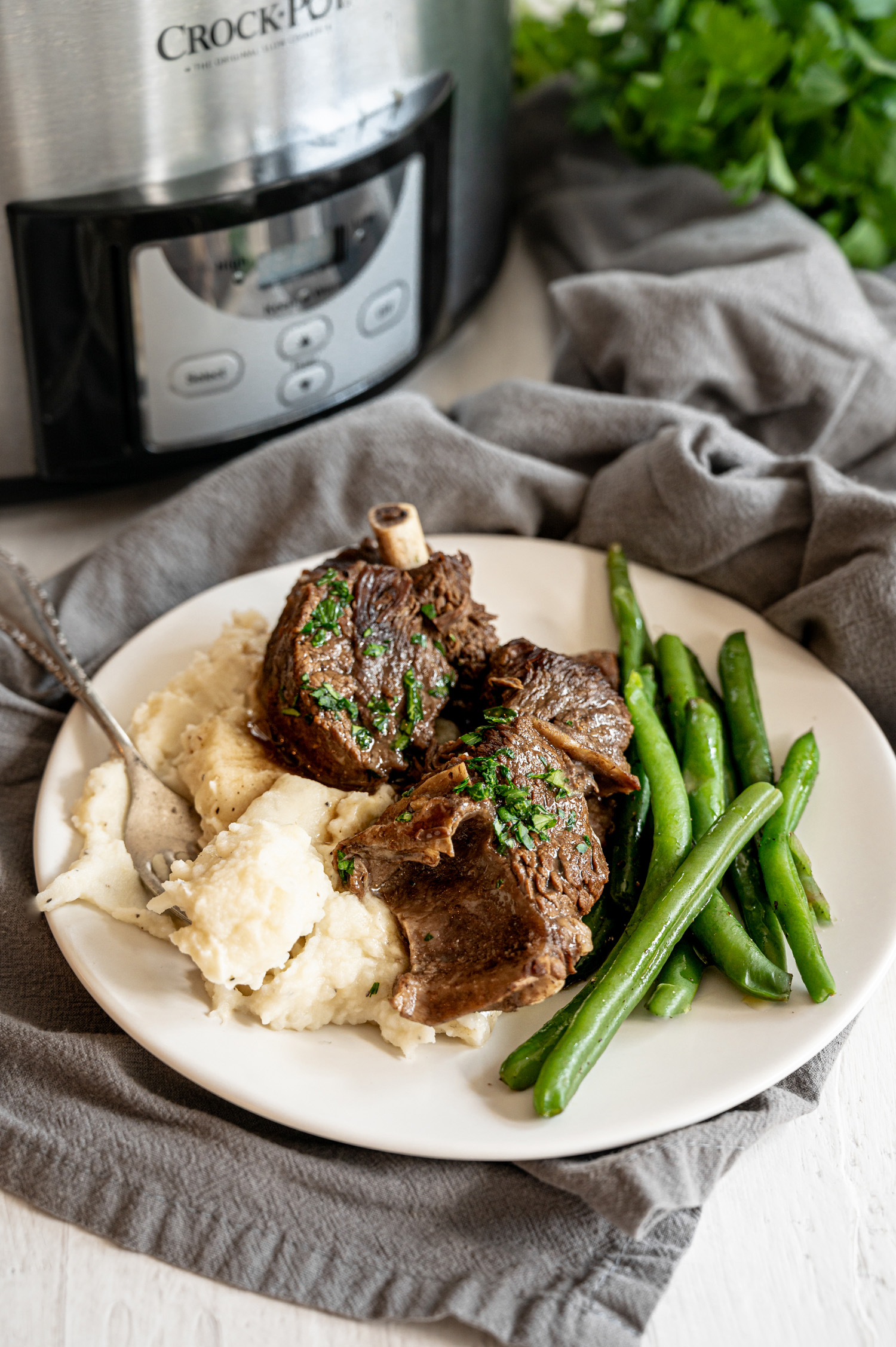 Slow Cooker short ribs on plate with mashed potatoes and green beans in front of a Crockpot.