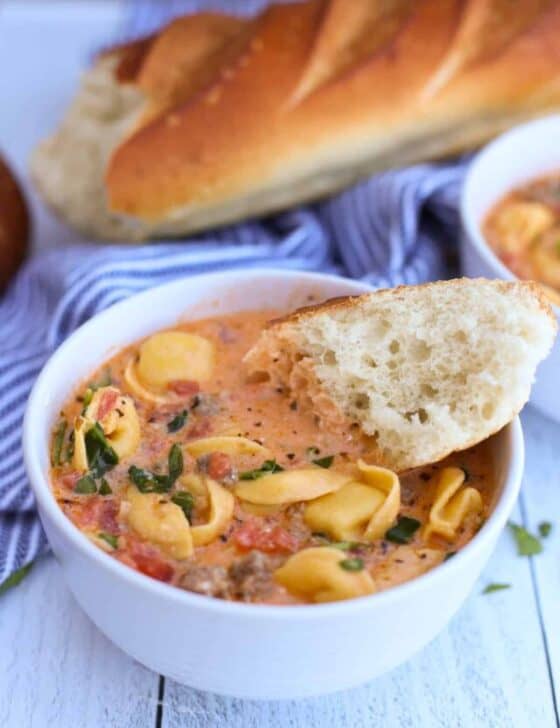 Sausage and tortellini soup in a white bowl with baguette