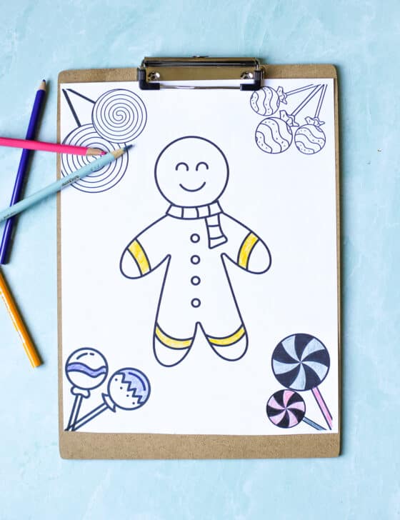 Partially colored gingerbread man coloring sheet on a clipboard with colored pencils scattered around.