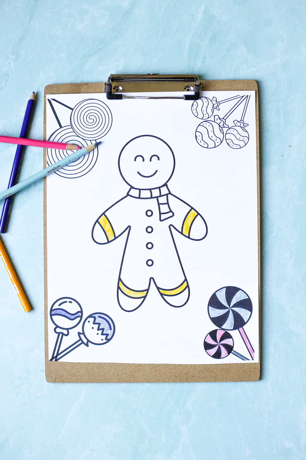 Gingerbread man coloring page on a clipboard with colored pencils around it.
